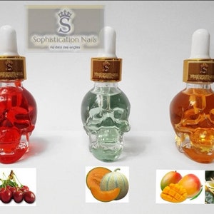 May include: Three glass bottles shaped like skulls filled with colored liquids. The bottles have gold lids with a crown and the text "Sophistication Nails Au dela des ongles". The bottles are arranged from left to right with red, green, and orange liquids. Below the bottles are three images of fruit: cherries, cantaloupe, and mango.