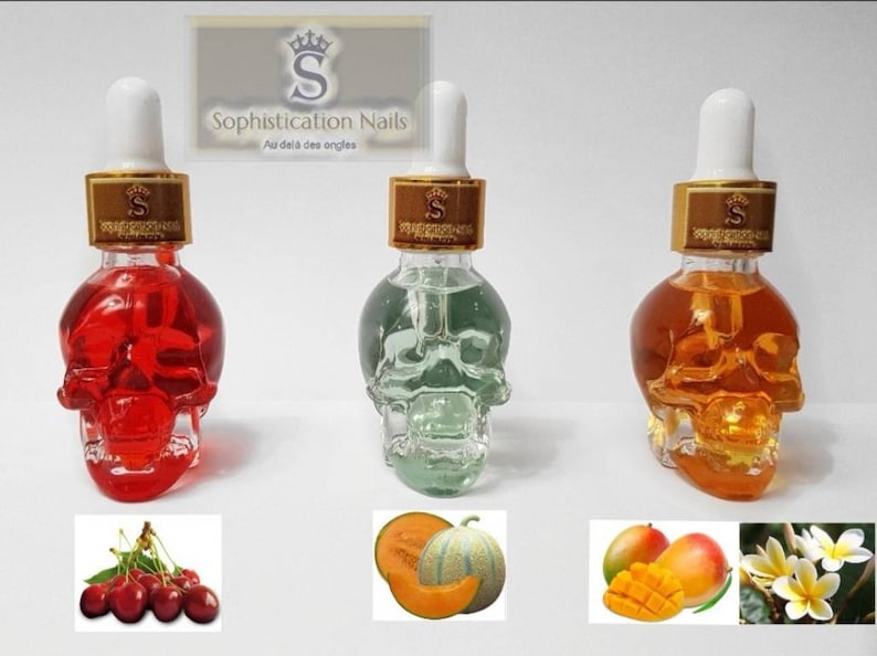 May include: Three glass bottles shaped like skulls filled with colored liquids. The bottles have gold lids with a crown and the text "Sophistication Nails Au dela des ongles". The bottles are arranged from left to right with red, green, and orange liquids. Below the bottles are three images of fruit: cherries, cantaloupe, and mango.