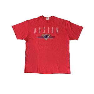 May include: Red short-sleeved t-shirt with a white graphic print of the word "BOSTON" and a stylized anchor design.