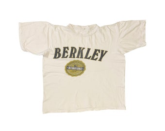 May include: A white t-shirt with a black and gold graphic that says "BERKLEY" and "INTERNATIONAL" with a crown above the word "INTERNATIONAL".