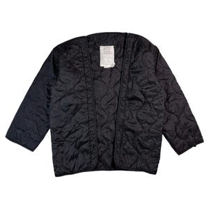 May include: Black quilted jacket with a diamond pattern. The jacket has a button-up front and long sleeves. A tag is visible near the collar. This jacket is a versatile outerwear piece.