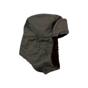 Puede incluir: Un gorro de cazador verde oliva oscuro con orejeras y forro de piel sintética. El gorro tiene tres ojales en el lateral y un cierre de velcro. Las orejeras se pueden asegurar con una correa de velcro.