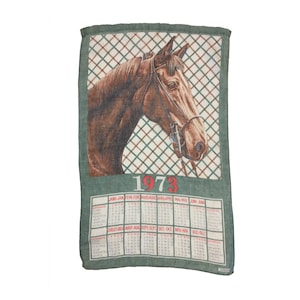 Puede incluir: Una toalla de cocina verde con una ilustraci&oacute;n de cabeza de caballo marr&oacute;n y un calendario para el a&ntilde;o 1973. El calendario est&aacute; en franc&eacute;s e incluye los meses de enero a diciembre.