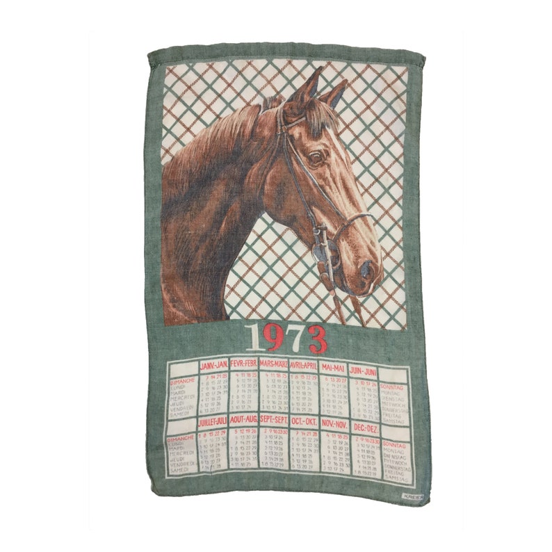 Puede incluir: Una toalla de cocina verde con una ilustraci&oacute;n de cabeza de caballo marr&oacute;n y un calendario para el a&ntilde;o 1973. El calendario est&aacute; en franc&eacute;s e incluye los meses de enero a diciembre.