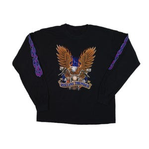 Puede incluir: Camiseta negra de manga larga con un diseño de motocicleta, águila y el texto "Rolling Thunder". El águila tiene alas marrones y está centrada sobre la motocicleta. Llamas moradas y azules en las mangas.