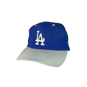May include: A blue and grey baseball cap with the LA logo embroidered in white on the front.
