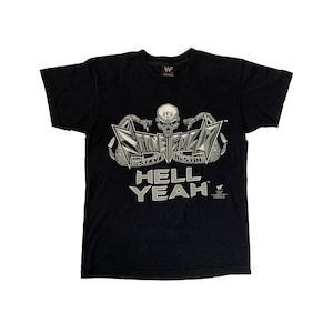 Puede incluir: Camiseta negra con un gráfico blanco de una calavera con serpientes y el texto "Stone Cold Steve Austin" y "Hell Yeah".