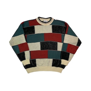 Op de afbeelding: Een veelkleurige trui met een geometrisch patroon in tinten rood, zwart, wit en blauw.