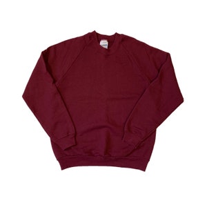 May include: A maroon crew neck sweatshirt with long sleeves and a raglan style.