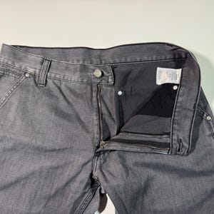 Peut inclure: Pantalon de travail en jean gris avec fermeture &eacute;clair, bouton et poches avant. Le pantalon a une conception classique &agrave; cinq poches et est fait d'un mat&eacute;riau en denim durable. Le pantalon est montr&eacute; d&eacute;boutonn&eacute; et d&eacute;zipp&eacute;.