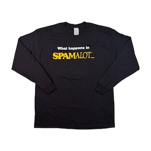 Puede incluir: Camiseta negra de manga larga con el texto "What happens in SPAMALOT..." en blanco y amarillo. La camiseta tiene cuello redondo y mangas largas. La camiseta está hecha de un material suave.