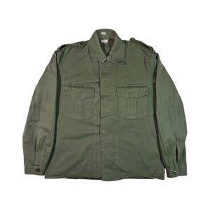 Puede incluir: Chaqueta verde oliva de estilo militar con dos bolsillos en el pecho y cierre de botones. La chaqueta de manga larga tiene cuello y charreteras en los hombros. La chaqueta está hecha de tela duradera.