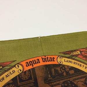 Puede incluir: Un pa&ntilde;o de cocina verde con un dise&ntilde;o marr&oacute;n y naranja. El dise&ntilde;o presenta un reloj, una espiga de trigo y el texto "aqua vitae", "Lang Syne?" y "For Auld Lang Syne".