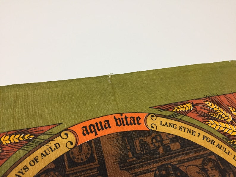 Puede incluir: Un pa&ntilde;o de cocina verde con un dise&ntilde;o marr&oacute;n y naranja. El dise&ntilde;o presenta un reloj, una espiga de trigo y el texto "aqua vitae", "Lang Syne?" y "For Auld Lang Syne".