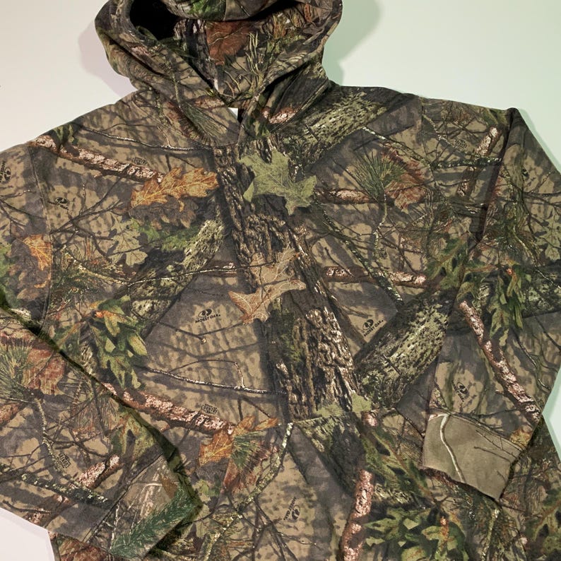 May include: A green, brown and tan camouflage hoodie with the words "Mossy Oak" printed on the front.