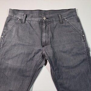 Peut inclure: Pantalon de travail en denim gris avec plusieurs poches et coutures renforc&eacute;es. Le pantalon a une fermeture boutonn&eacute;e et des rivets aux poches. Le tissu semble pr&eacute;-lav&eacute;. Un style de v&ecirc;tement de travail classique.