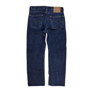 Könnte beinhalten: Eine dunkelblaue Jeans mit klassischer gerader Passform. Die Jeans hat ein rotes Etikett auf der Gesäßtasche mit dem Levi's-Logo.