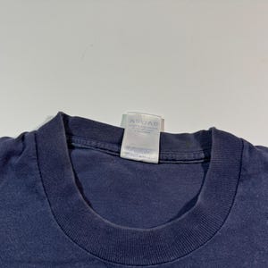 May include: A navy blue t-shirt with a white care tag attached to the neck. The tag has instructions for washing and drying the shirt.