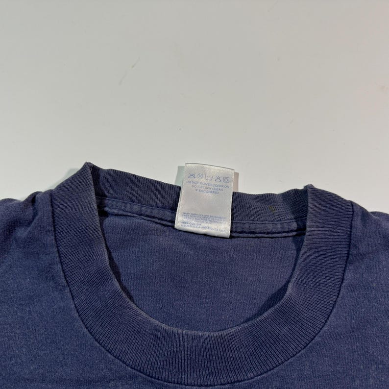 May include: A navy blue t-shirt with a white care tag attached to the neck. The tag has instructions for washing and drying the shirt.