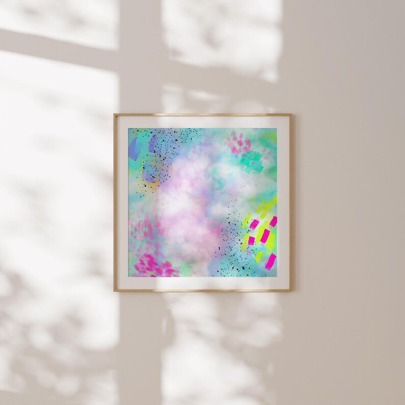 May include: Abstract art print with a colorful, layered design featuring pink, blue, green, yellow, and black paint splatters and brushstrokes. The print is framed in a light wood frame.
