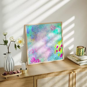 May include: A framed abstract painting with a light blue, pink, and yellow background. The painting has a splattered effect with black, pink, and green accents.