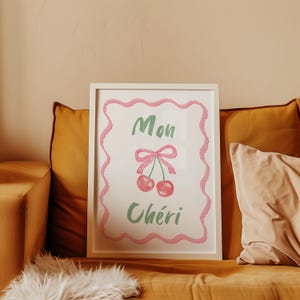 May include: A white framed print with a pink and green design. The print features two red cherries with a green stem and a pink bow. The text "Mon Chéri" is written in green cursive.
