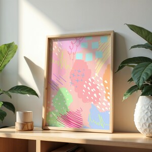 Könnte beinhalten: Ein gerahmter abstrakter Kunstdruck mit rosa Hintergrund und bunten geometrischen Formen, Linien und Punkten. Der Druck ist in einem hellen Holzrahmen.