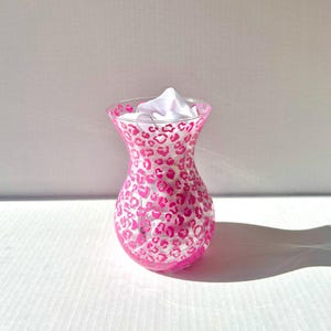 May include: A clear glass vase with a pink leopard print design. The vase is empty and has a wide mouth.