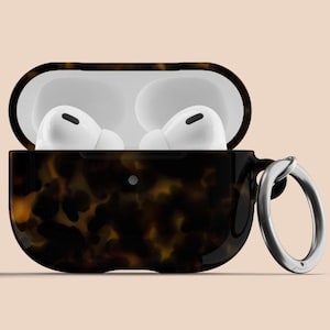 May include: A tortoiseshell patterned case for wireless earbuds with a silver ring attached. The case is open and the earbuds are inside.