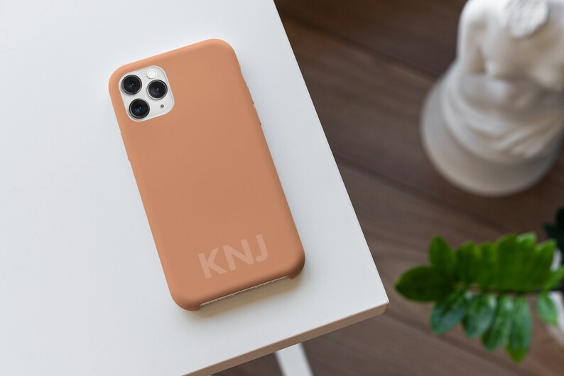 May include: A light brown phone case with a white camera lens and the letters "KNJ" printed on the back.