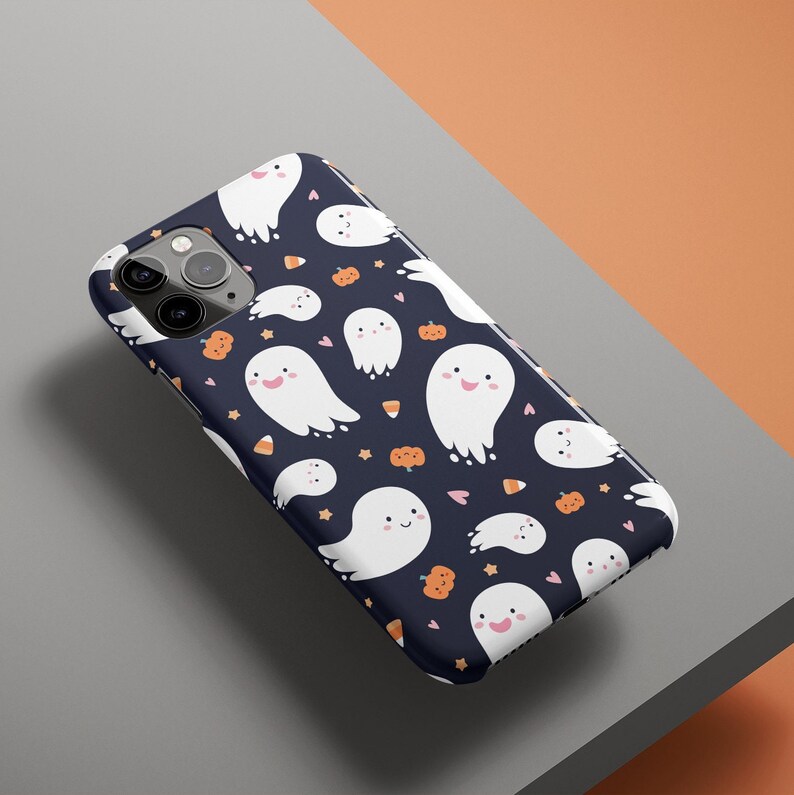 May include: A black phone case with a pattern of white ghosts, orange pumpkins, and candy corn on a dark blue background.