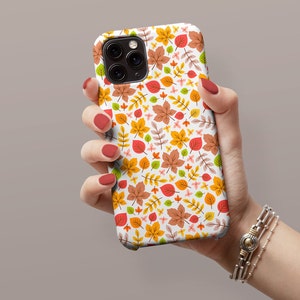May include: A white iPhone case with a colorful autumn leaf pattern. The case features a variety of leaves in shades of orange, yellow, red, and green.