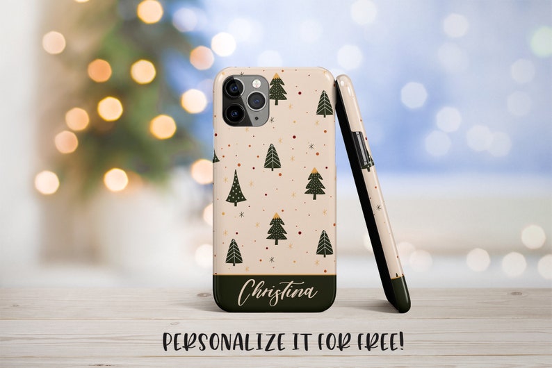 K&ouml;nnte beinhalten: Eine personalisierte Handyh&uuml;lle mit cremefarbenem Hintergrund und einem Muster aus gr&uuml;nen Weihnachtsb&auml;umen, roten und goldenen Punkten und Schneeflocken. Der Text "Christina" ist in Schwarz am unteren Rand der H&uuml;lle aufgedruckt.