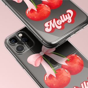 May include: Clear phone cases with a watercolor design of red cherries and pink bows. The name "Molly" is written in a retro font on each case. The cases are shown on a pink background.