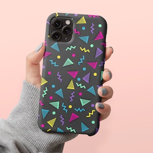 May include: A black phone case with a vibrant 80s-inspired geometric pattern. The design features colorful triangles, zigzags, and circles in shades of pink, yellow, blue, and purple. The case is designed to fit a smartphone.