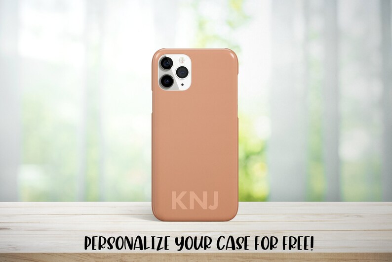 May include: A peach-colored phone case with a white camera bump and the initials "KNJ" printed on the back.  Personalize your case for free!