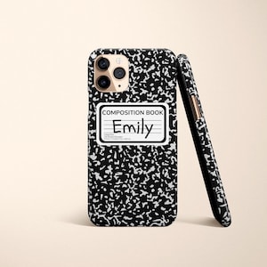 May include: Black and white composition notebook phone case with a white label that says "COMPOSITION BOOK" and "Emily" in black handwriting.