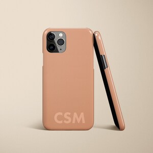 May include: A peach-colored phone case with a camera lens cutout and the initials "CSM" printed on the back.