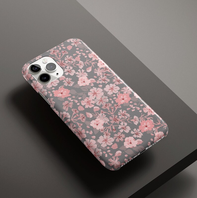 Puede incluir: Una funda de tel&eacute;fono blanca con un patr&oacute;n floral. Las flores son rosas y blancas y est&aacute;n dispuestas en un patr&oacute;n repetitivo. La funda est&aacute; dise&ntilde;ada para un iPhone.