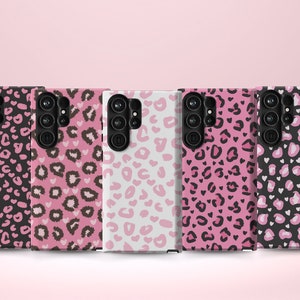 May include: Five different phone cases with a pink and black leopard print design. The cases are all lined up in a row on a pink background.