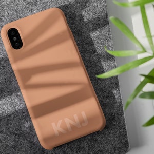 May include: A peach-colored phone case with the letters "KNJ" printed in white on the back.