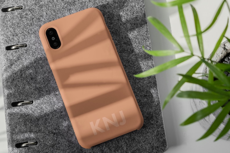 May include: A peach-colored phone case with the letters "KNJ" printed in white on the back.