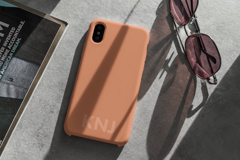 May include: A peach-colored phone case with the letters "KNJ" printed on the back.