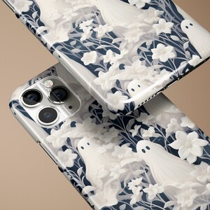 May include: Two white iPhone cases with a dark blue background and a white floral pattern with white ghost figures.