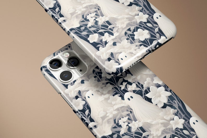 May include: Two white iPhone cases with a dark blue background and a white floral pattern with white ghost figures.