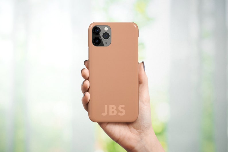May include: A light brown phone case with a black camera lens and the initials "JBS" printed on the back.
