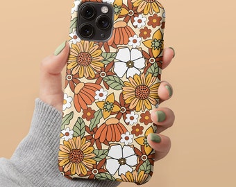 May include: A phone case with a retro floral design. The case features a pattern of sunflowers, white flowers, and other floral elements in shades of orange, yellow, and brown against a cream background. The case is held by a person.
