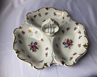 Puede incluir: Un plato de servir de porcelana blanca con tres secciones y un borde dorado. El plato está decorado con un patrón floral en tonos de rosa, morado, azul y amarillo.