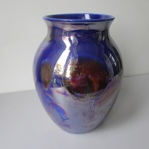 Könnte beinhalten: Eine blaue Keramikvase mit einem irisierenden Überzug. Der Überzug hat einen metallischen Glanz und erzeugt einen Regenbogeneffekt.