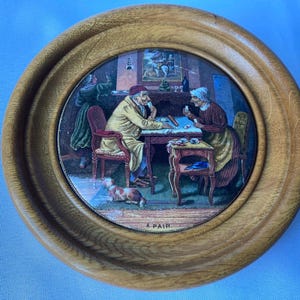 Pode incluir: Uma imagem oval emoldurada em madeira que representa uma cena pintada de duas pessoas jogando cartas. A imagem é intitulada "A Pair".